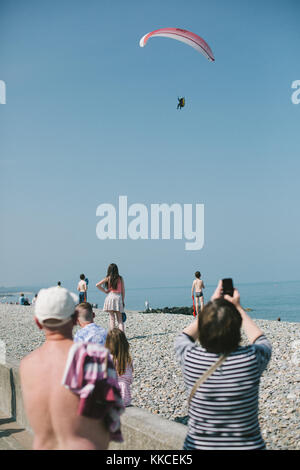 People watching parachute flight over Bray`s stony beach on a sunny May day. Bray, Wicklow, Ireland Stock Photo